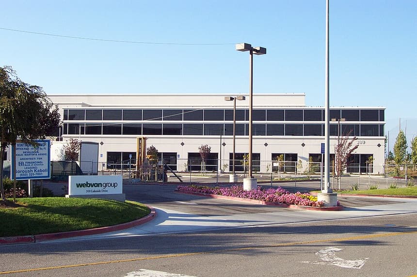 A low white office building behind a temporary fence, with a Webvan Group sign at the driveway